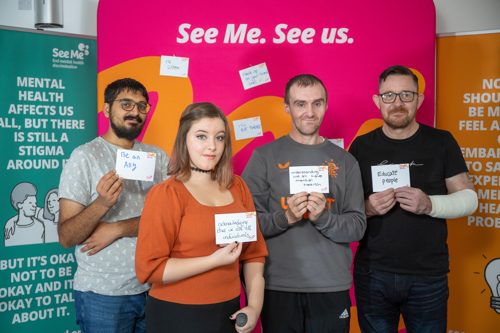 Four See Me volunteers hold up postcards reading what they'll do to tackle stigma - 'Be an ally'; 'acknowledge that we are all individuals'; 'understanding we all have mental health'; 'educate people'