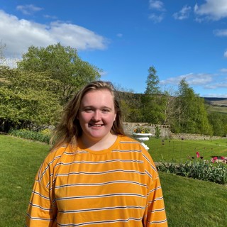 A young woman, Nicky, stands in a garden, smiling at the camera.